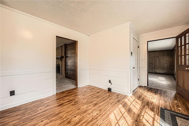 empty room featuring wood finished floors, ornamental molding, a fireplace, and a textured ceiling