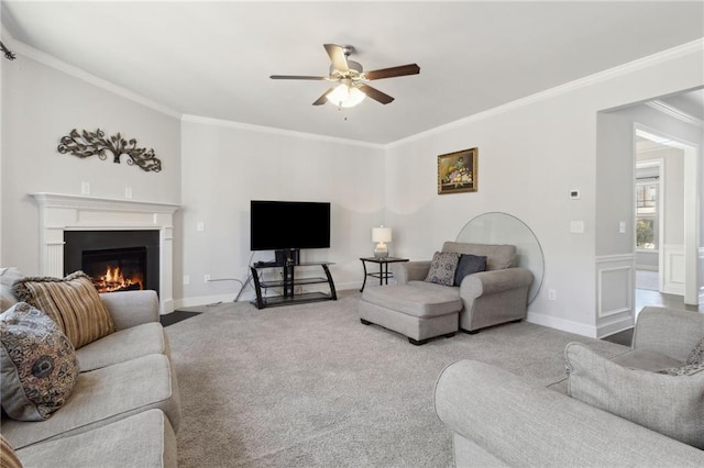 living area featuring ceiling fan, a fireplace with flush hearth, baseboards, ornamental molding, and carpet