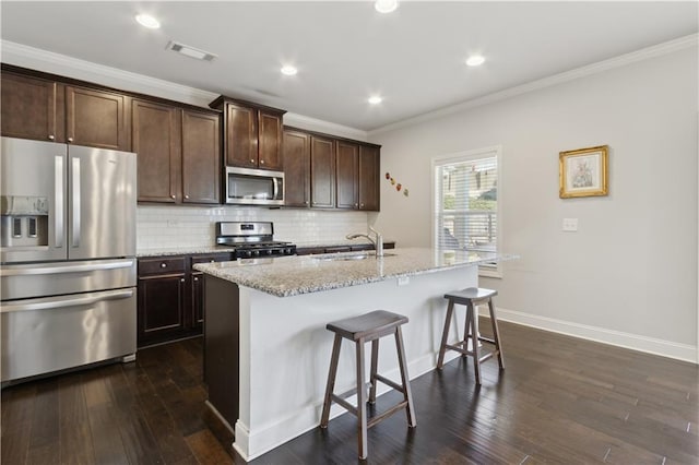 kitchen featuring visible vents, backsplash, appliances with stainless steel finishes, a kitchen island with sink, and light stone countertops