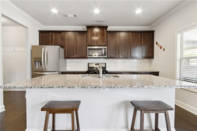 kitchen with stainless steel appliances, a center island with sink, a sink, and visible vents