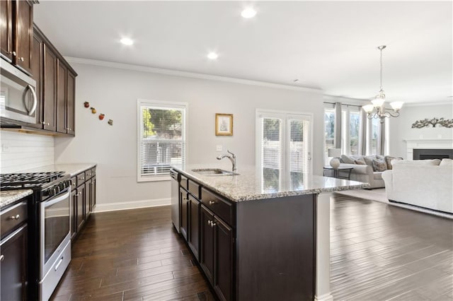 kitchen with dark brown cabinetry, a center island with sink, appliances with stainless steel finishes, open floor plan, and a sink