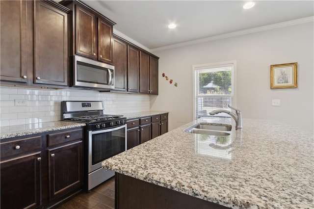 kitchen featuring stainless steel appliances, a kitchen island with sink, a sink, dark brown cabinets, and light stone countertops