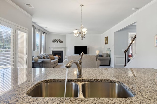 kitchen with light stone countertops, ornamental molding, open floor plan, and a sink