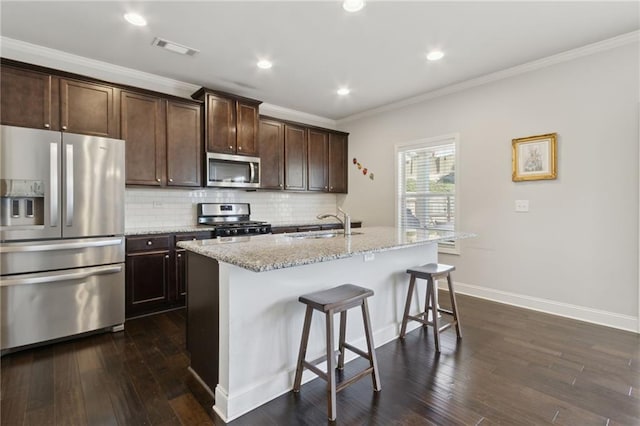 kitchen with tasteful backsplash, visible vents, appliances with stainless steel finishes, light stone countertops, and a kitchen island with sink