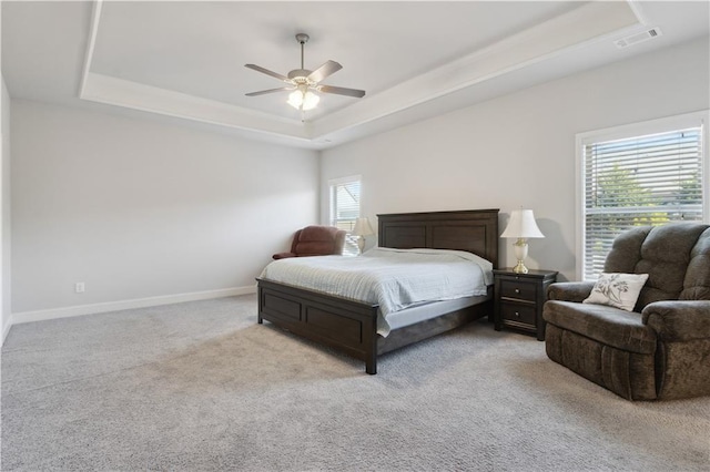 bedroom with baseboards, visible vents, a ceiling fan, light colored carpet, and a tray ceiling