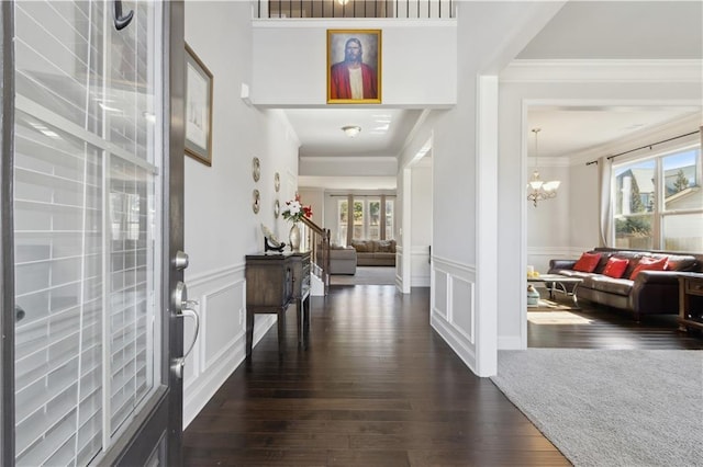 entrance foyer with a chandelier, a decorative wall, ornamental molding, wainscoting, and dark wood-style floors