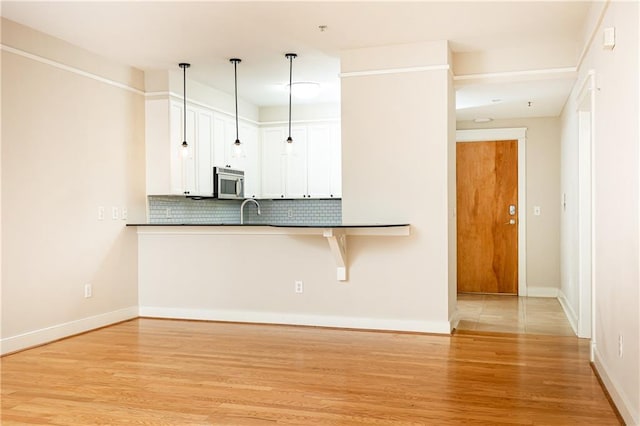 kitchen with decorative backsplash, light wood-type flooring, white cabinetry, and hanging light fixtures