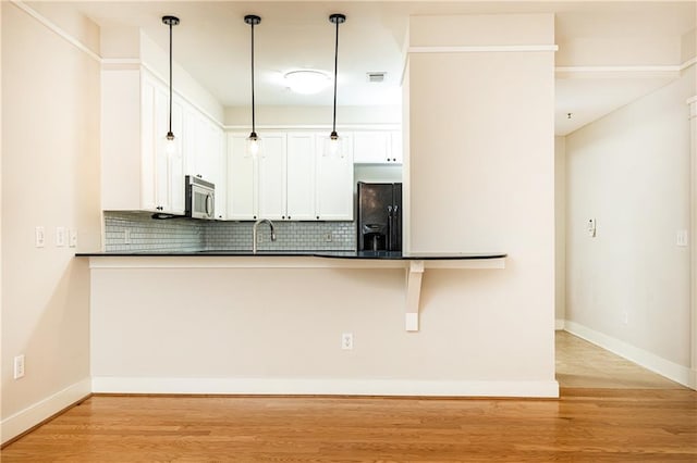 kitchen with hanging light fixtures, backsplash, black fridge with ice dispenser, white cabinets, and light wood-type flooring