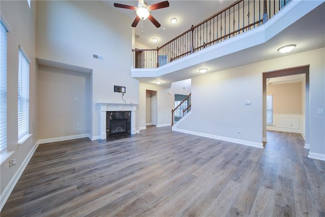 unfurnished living room featuring wood-type flooring, a tile fireplace, and a high ceiling