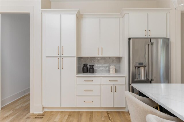 kitchen featuring light countertops, light wood-style flooring, decorative backsplash, wall chimney range hood, and high end stove