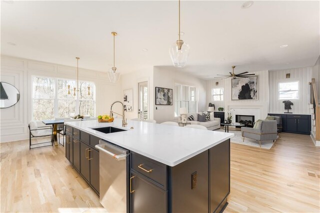 kitchen featuring a fireplace, a sink, dishwasher, light wood finished floors, and an island with sink