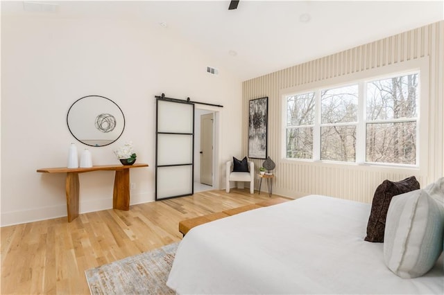 bedroom featuring a barn door, visible vents, baseboards, and wood finished floors