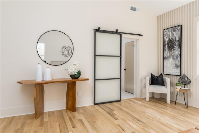 unfurnished room featuring wood finished floors, visible vents, baseboards, and a barn door