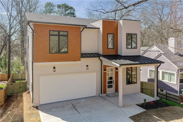 contemporary home featuring driveway, metal roof, an attached garage, a standing seam roof, and fence