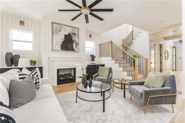 living room with a ceiling fan, wood finished floors, a premium fireplace, and stairs