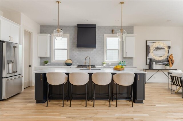 kitchen with white cabinets, light countertops, high quality fridge, and an island with sink