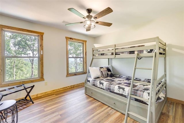 bedroom with a ceiling fan, visible vents, baseboards, and wood finished floors