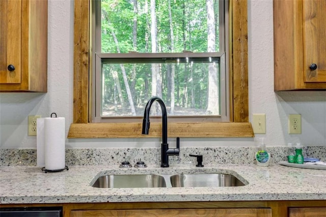 kitchen with light stone countertops, brown cabinets, and a sink