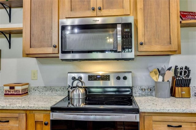 kitchen with open shelves, appliances with stainless steel finishes, brown cabinetry, and light stone countertops