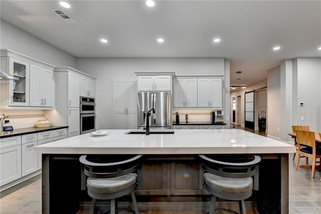 kitchen with a large island with sink, appliances with stainless steel finishes, a kitchen breakfast bar, a barn door, and glass insert cabinets