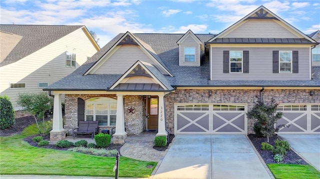 craftsman-style house featuring stone siding, a standing seam roof, a front lawn, and concrete driveway