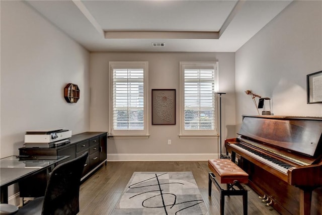 office with dark wood-type flooring, a tray ceiling, and a healthy amount of sunlight