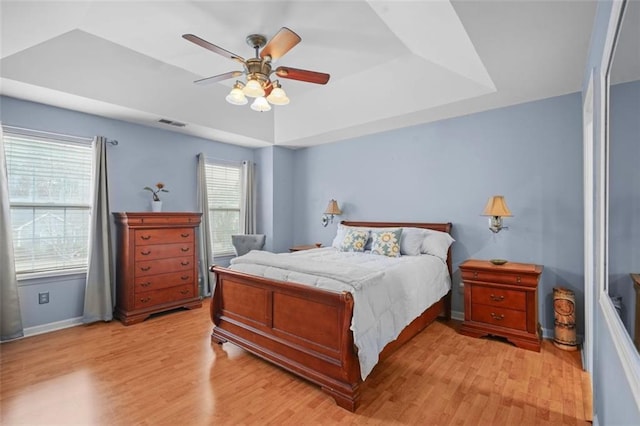 bedroom featuring visible vents, baseboards, a ceiling fan, light wood finished floors, and a raised ceiling