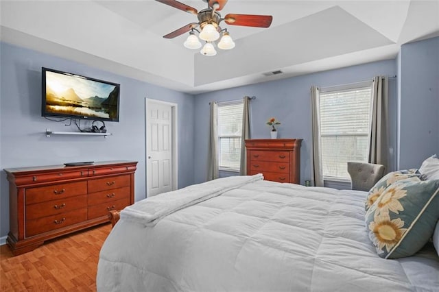 bedroom with ceiling fan, a raised ceiling, visible vents, and light wood-style floors