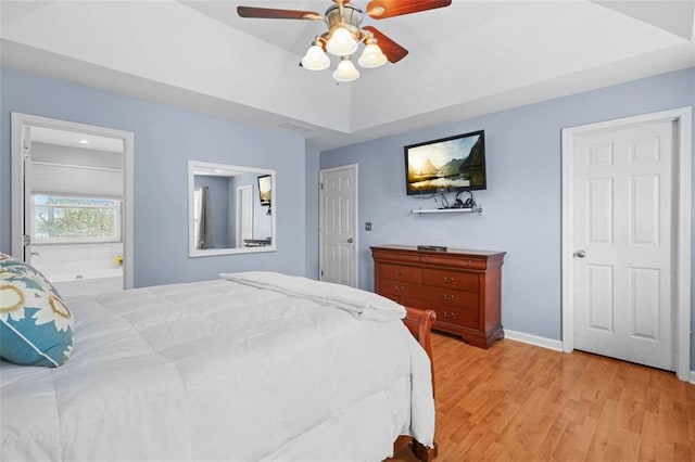 bedroom featuring light wood finished floors, baseboards, a tray ceiling, and ceiling fan