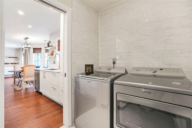 clothes washing area featuring laundry area, wood finished floors, washing machine and clothes dryer, a sink, and tile walls