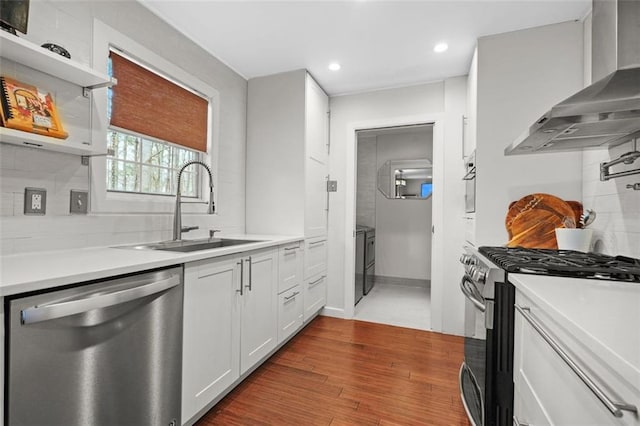 kitchen with stainless steel appliances, a sink, wall chimney range hood, decorative backsplash, and dark wood finished floors