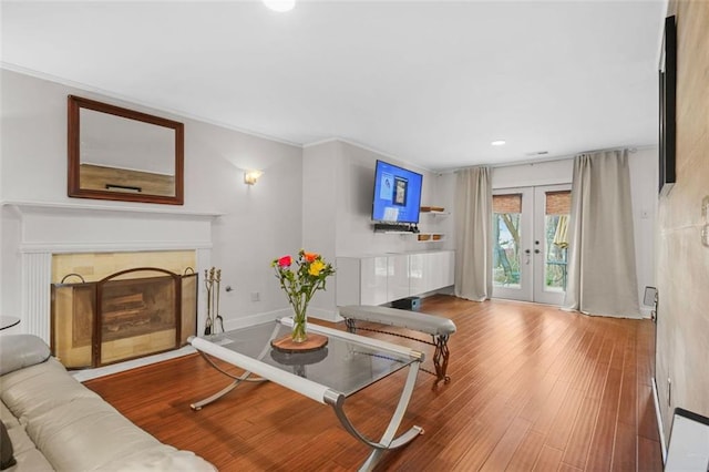 living room featuring baseboards, a tiled fireplace, wood finished floors, crown molding, and french doors