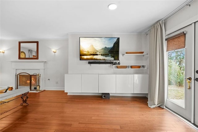 unfurnished living room with a lit fireplace, baseboards, light wood-style flooring, and crown molding