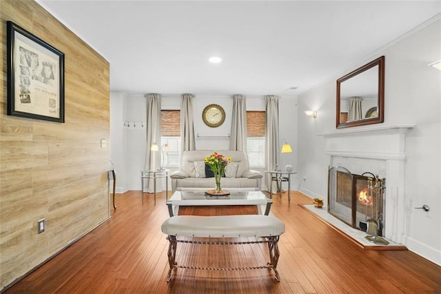 living area with hardwood / wood-style flooring, a lit fireplace, baseboards, and wood walls