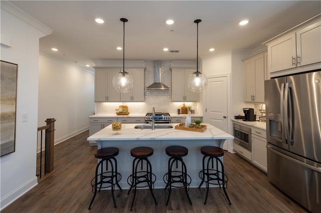 kitchen with wall chimney exhaust hood, stainless steel appliances, pendant lighting, dark hardwood / wood-style floors, and an island with sink