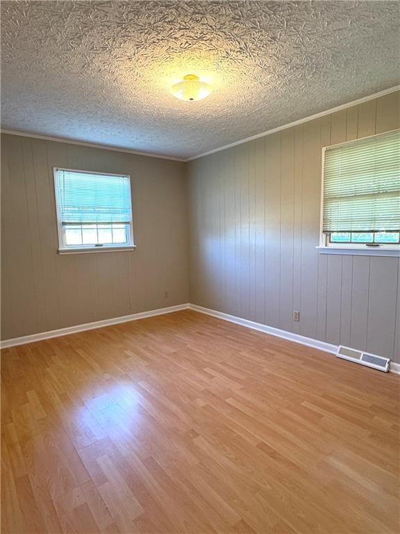 empty room featuring wood walls, light hardwood / wood-style floors, and a textured ceiling