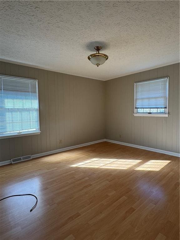 empty room with a healthy amount of sunlight, a textured ceiling, and light wood-type flooring