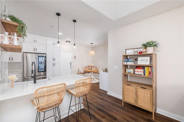 kitchen featuring dark wood-type flooring, stainless steel fridge, kitchen peninsula, pendant lighting, and white cabinets