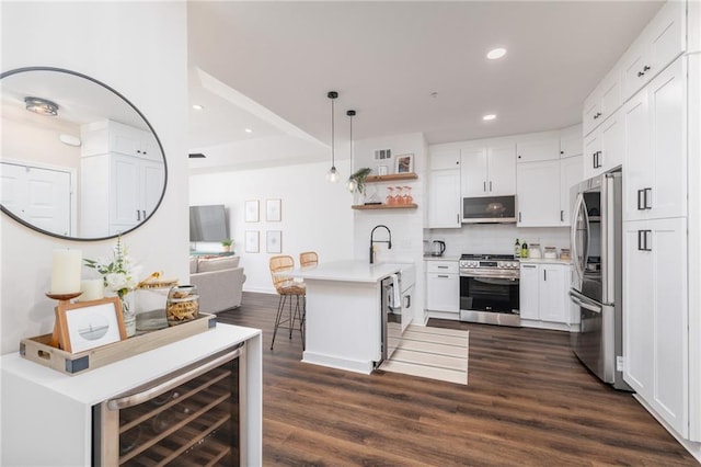 kitchen featuring appliances with stainless steel finishes, a breakfast bar area, white cabinets, hanging light fixtures, and dark wood-type flooring