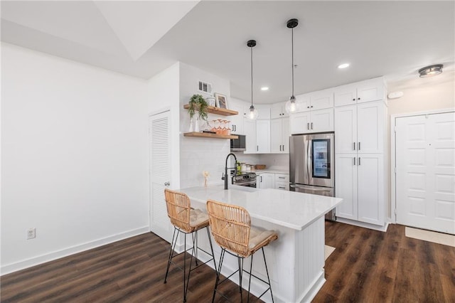 kitchen featuring lofted ceiling, a kitchen bar, kitchen peninsula, stainless steel appliances, and white cabinets