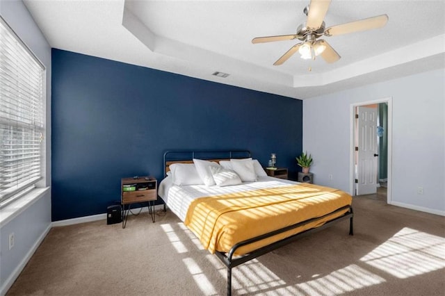 carpeted bedroom featuring ceiling fan and a raised ceiling