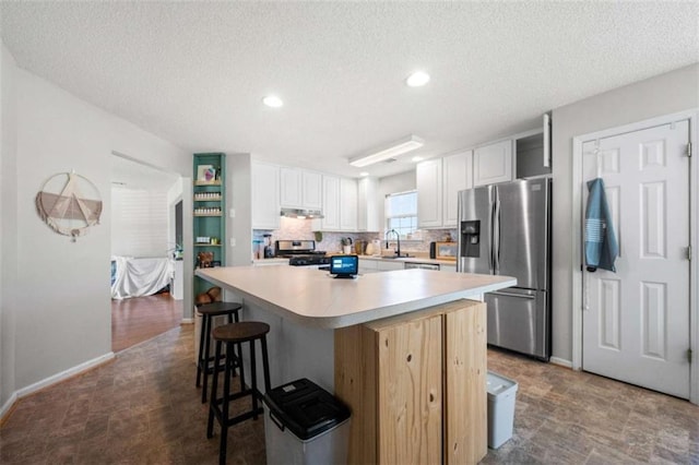 kitchen with a breakfast bar, appliances with stainless steel finishes, white cabinetry, tasteful backsplash, and a kitchen island