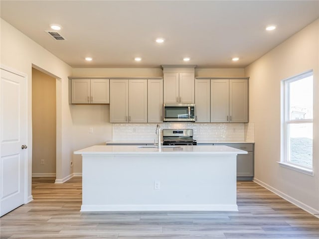 kitchen featuring gray cabinetry, a kitchen island with sink, sink, light wood-type flooring, and stainless steel appliances