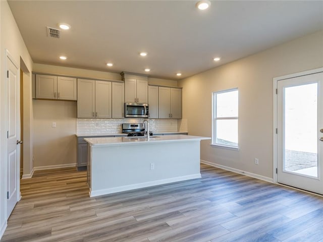 kitchen featuring gray cabinets, an island with sink, appliances with stainless steel finishes, and light hardwood / wood-style flooring