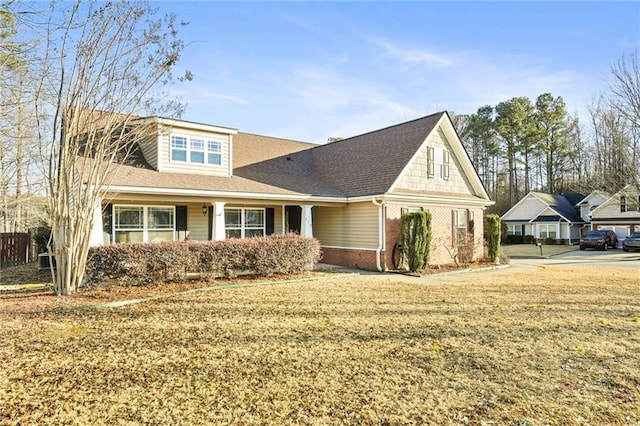 view of front of house with a shingled roof, brick siding, and a front lawn