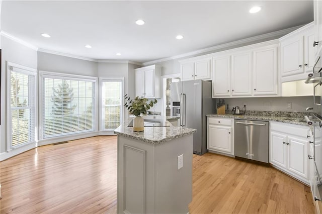 kitchen with white cabinets, appliances with stainless steel finishes, light stone counters, and a center island