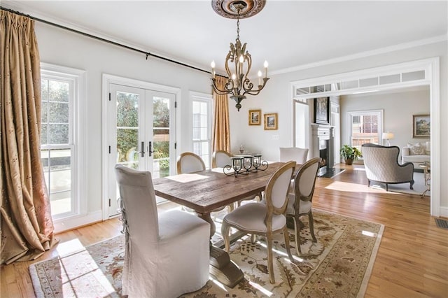 dining area featuring light wood-type flooring, ornamental molding, french doors, and a notable chandelier