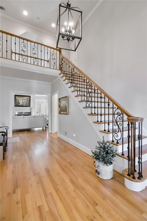 unfurnished living room featuring a high ceiling, an inviting chandelier, crown molding, and hardwood / wood-style flooring