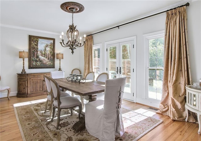 dining room featuring light hardwood / wood-style floors, ornamental molding, french doors, and an inviting chandelier