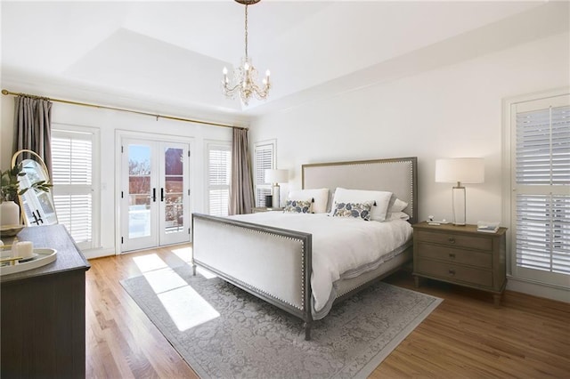 bedroom with an inviting chandelier, hardwood / wood-style flooring, a tray ceiling, access to exterior, and french doors